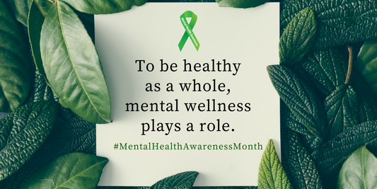 A card featuring a green mental health awareness ribbon and the text "To be healthy as a whole, mental wellness plays a role. #MentalHealthAwarenessMonth" laid over a background of lush green leaves.
