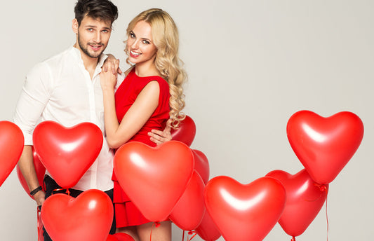 A smiling couple surrounded by red heart-shaped balloons.