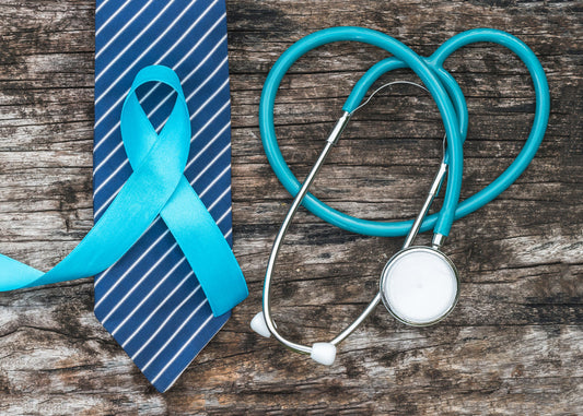 A light blue prostate cancer awareness ribbon laid across a blue and white striped necktie next to a stethoscope on a rustic wooden background.