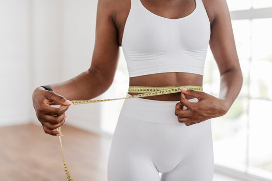 Women in white athletic wear measuring her waist with a yellow measuring tape.